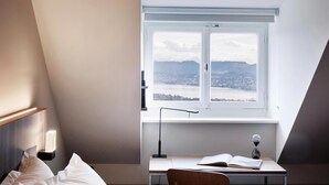 A bedroom with a bed, a desk with a chair, a window with a view, and a radiator. - Sorell Boutique-Hotel Zürichberg (Zürich)