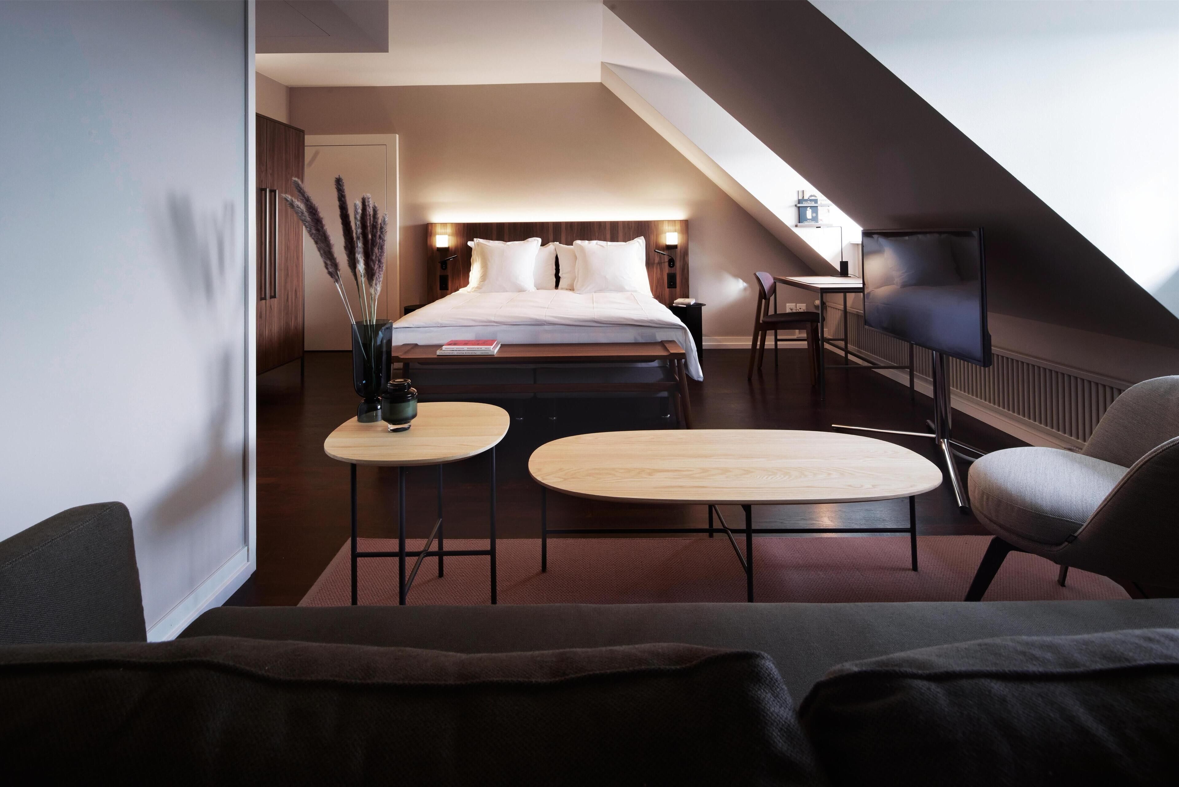 Ein modernes Hotelzimmer mit einem Bett, zwei kleinen Tischen, einer Couch und einem Fernseher.