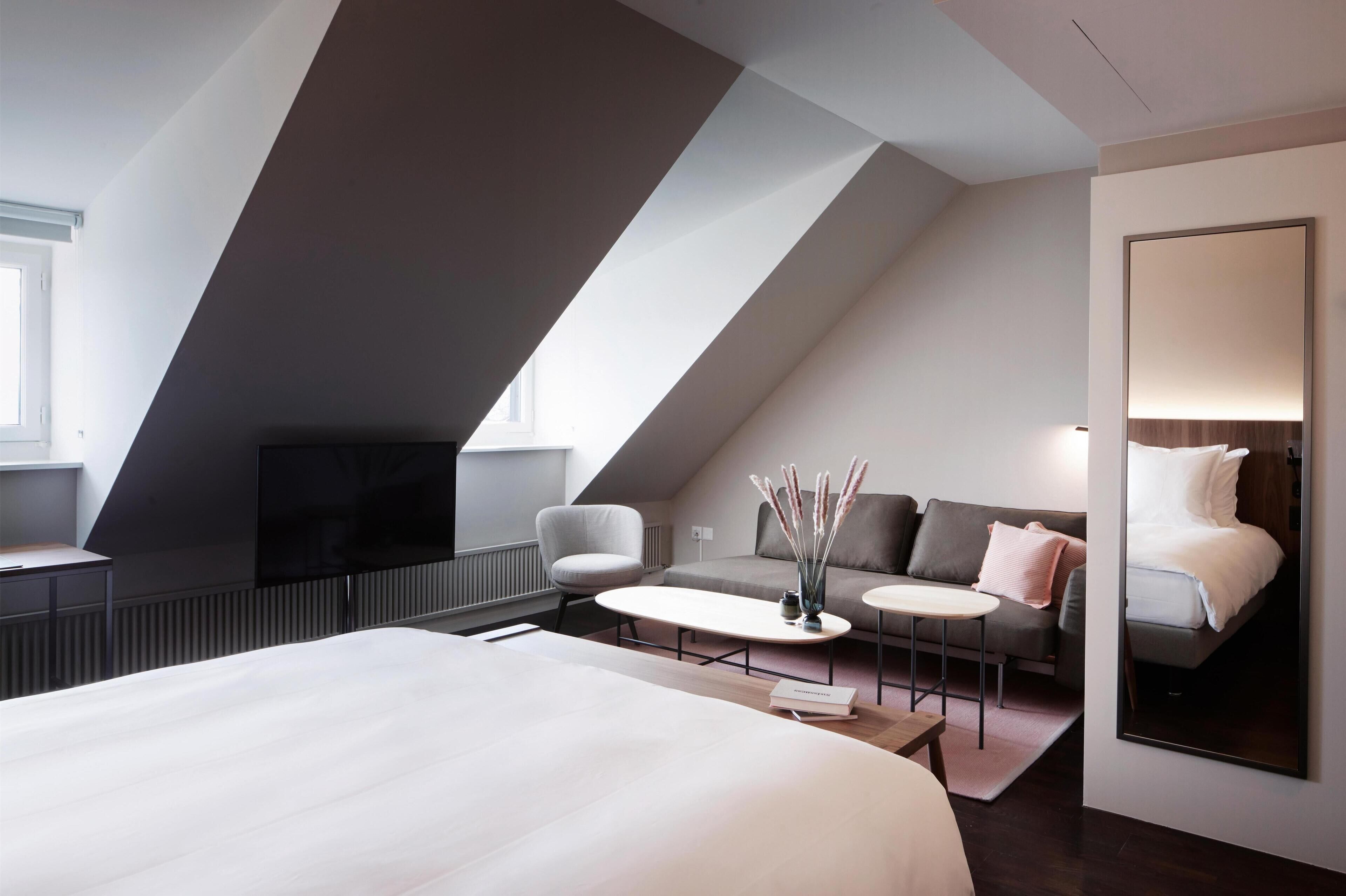 Een moderne hotelkamer met een groot bed, een flatscreen televisie, een bank, een klein bijzettafeltje en een grote spiegel.