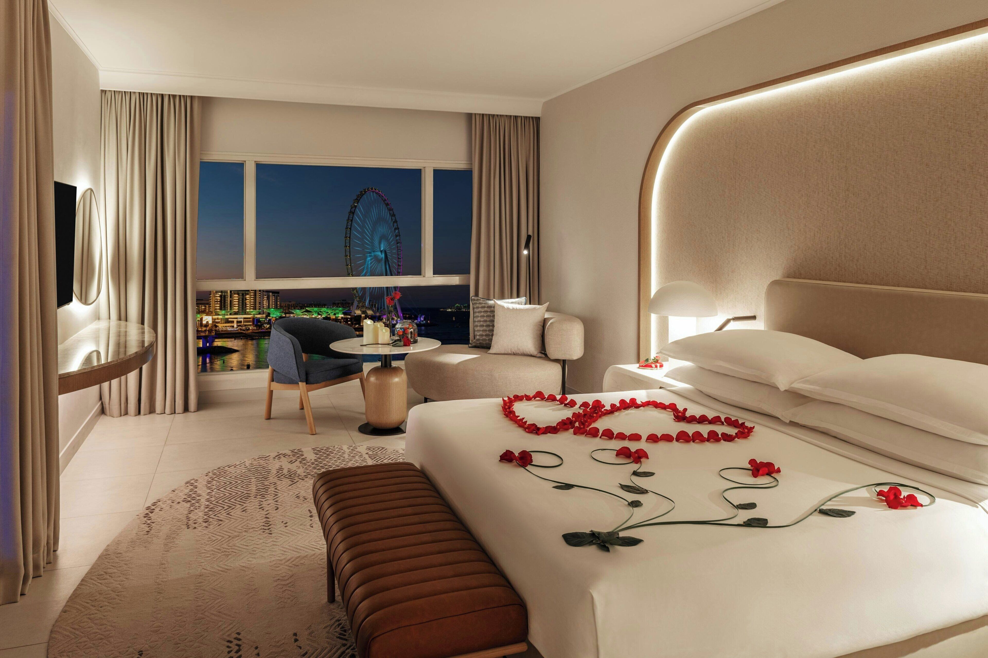 A modern hotel room with a large bed, a desk, and a view of a Ferris wheel at night.