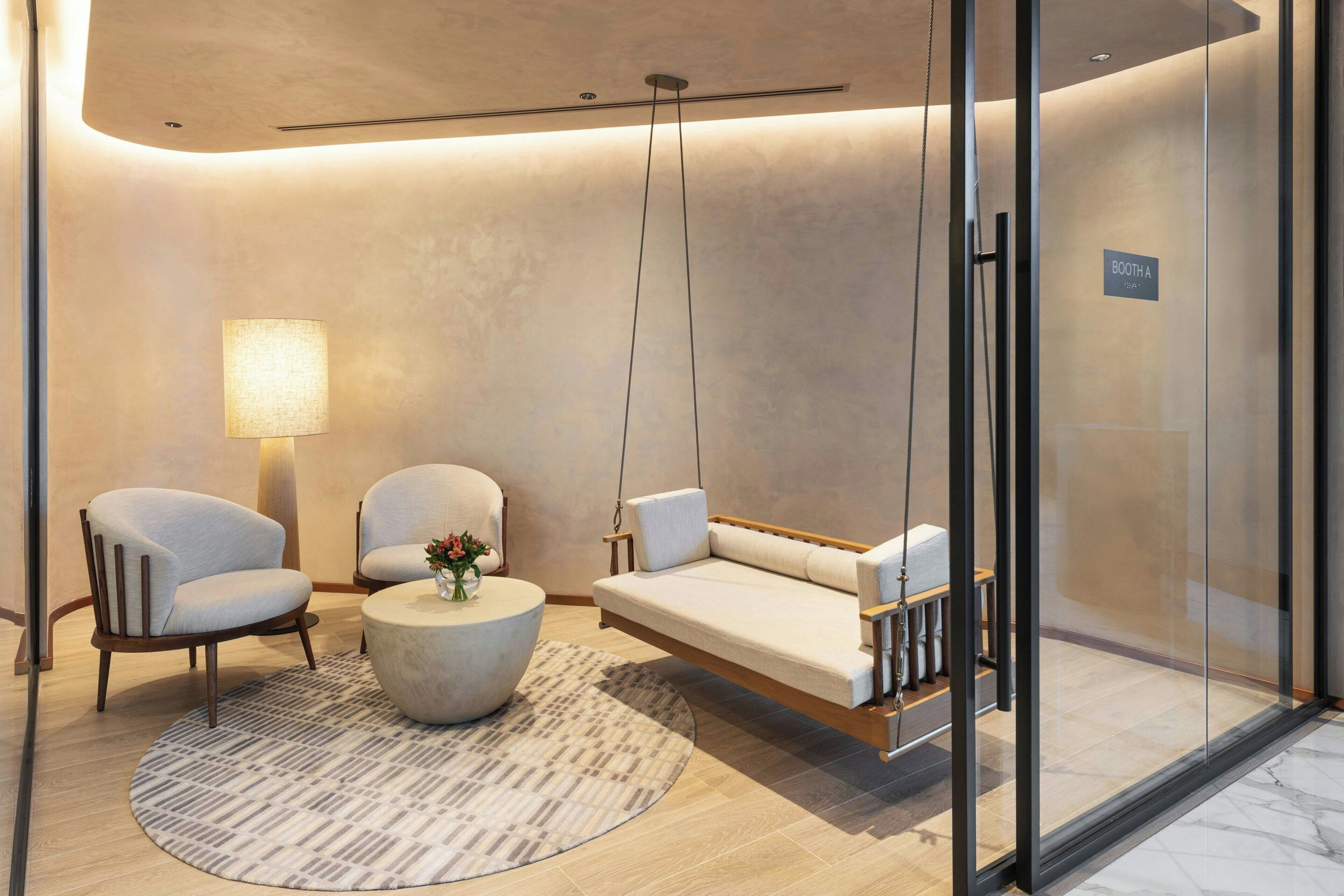 Un intérieur moderne avec une balançoire suspendue, deux fauteuils, une table basse ronde et une lampe.