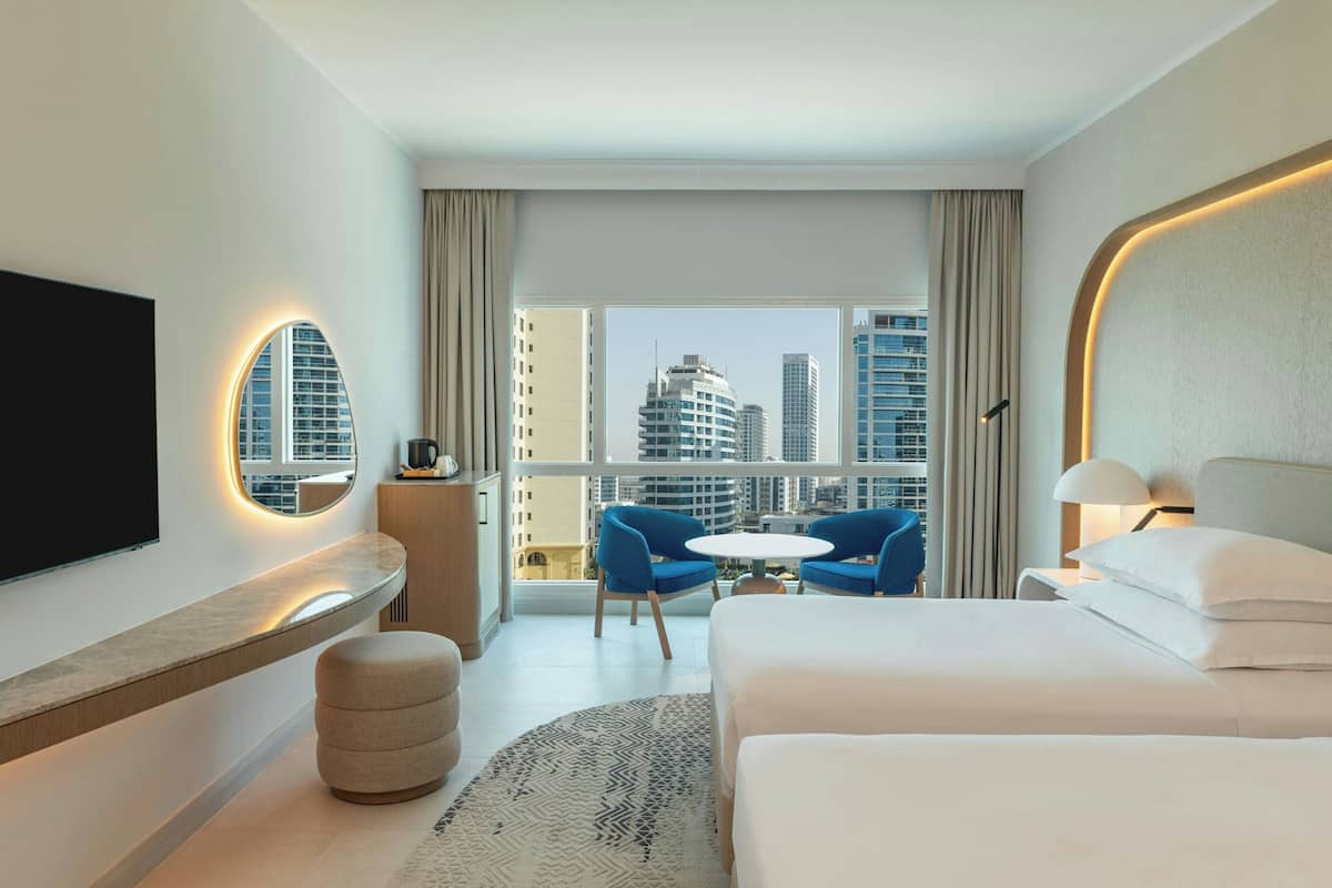 A modern hotel room with a large bed, a TV, a round table, and a balcony with city views.