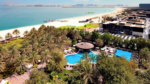 A resort with a swimming pool, beach, and palm trees.