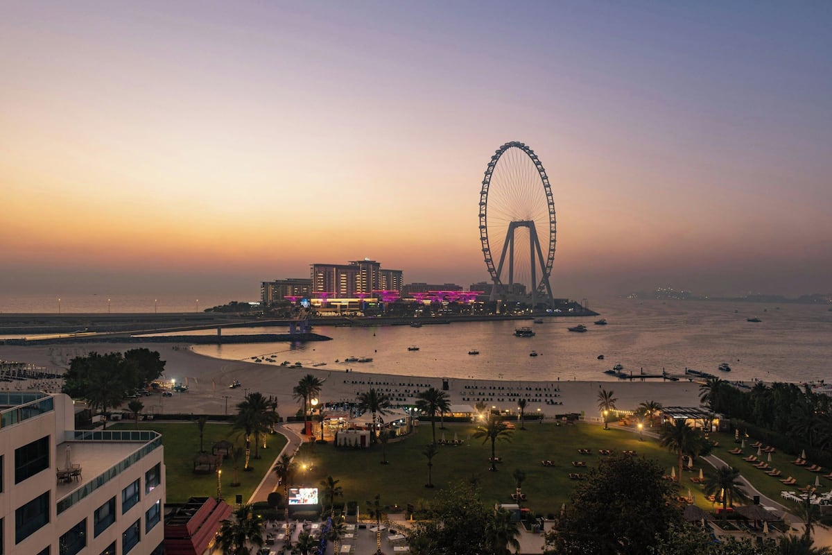 A waterfront view with a large Ferris wheel, a beach, and a building with illuminated windows.