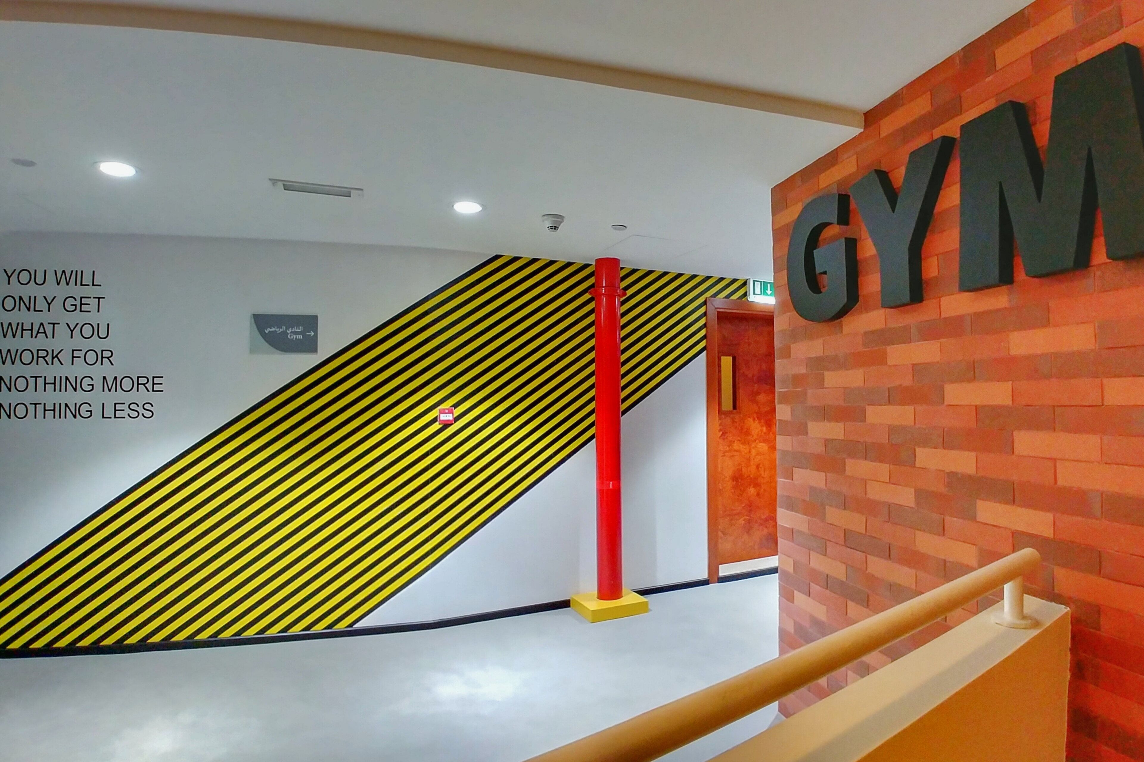 Een sportschool met een groot 'GYM' bord, een geel- en zwart gestreept muur en een rode pilaar.