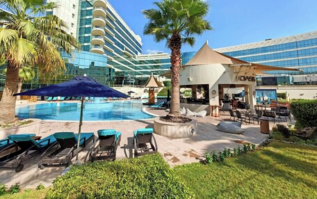 A hotel pool area with lounge chairs, a palm tree, and a building with a glass facade.