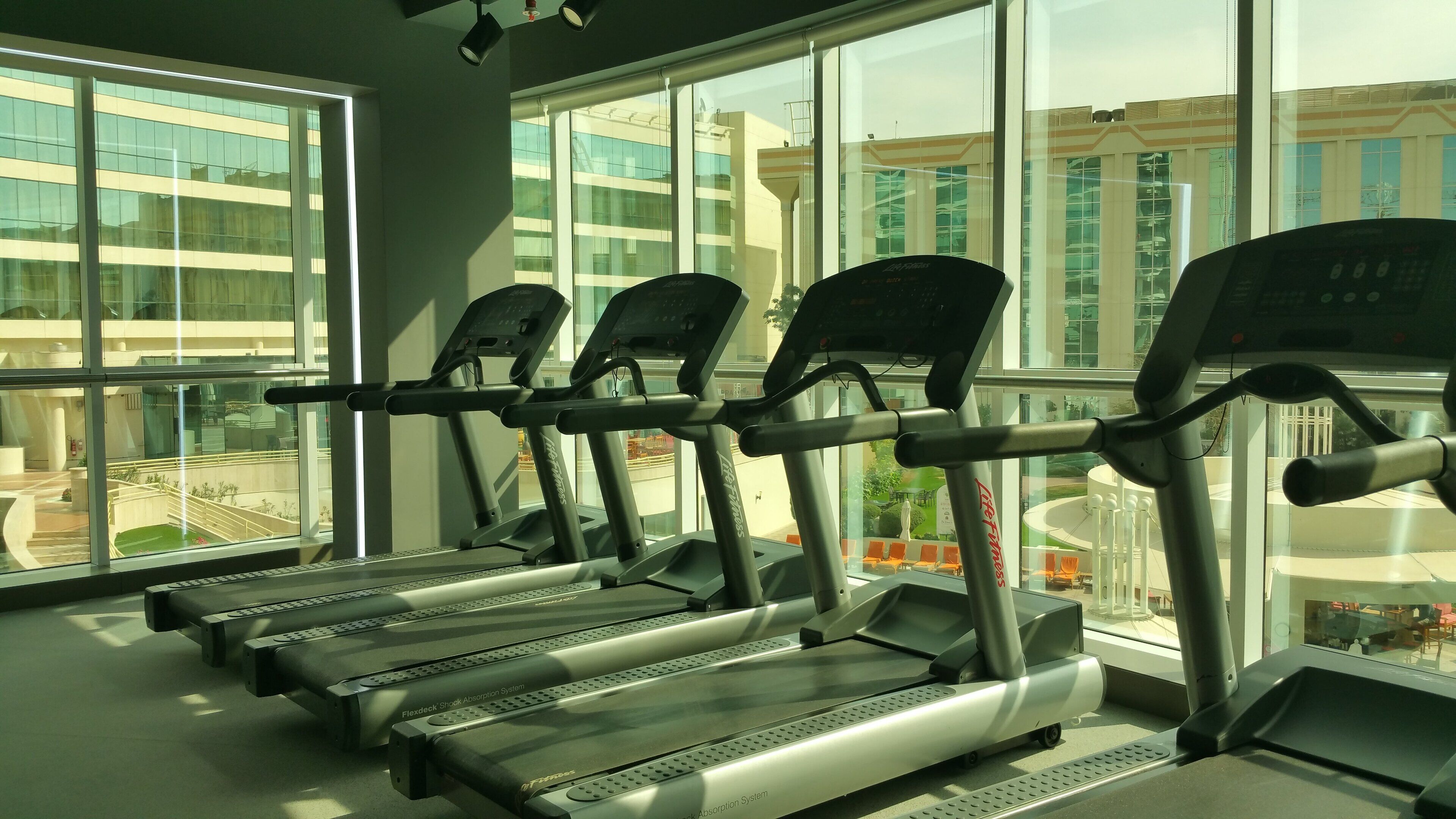 A gym with treadmills and a view of a cityscape through large windows.
