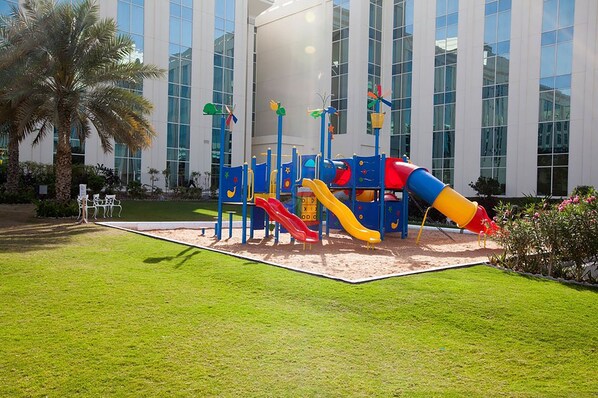 A playground with slides and climbing structures in front of a modern building with large windows. - Millennium Airport Hotel Dubai (Dubai)