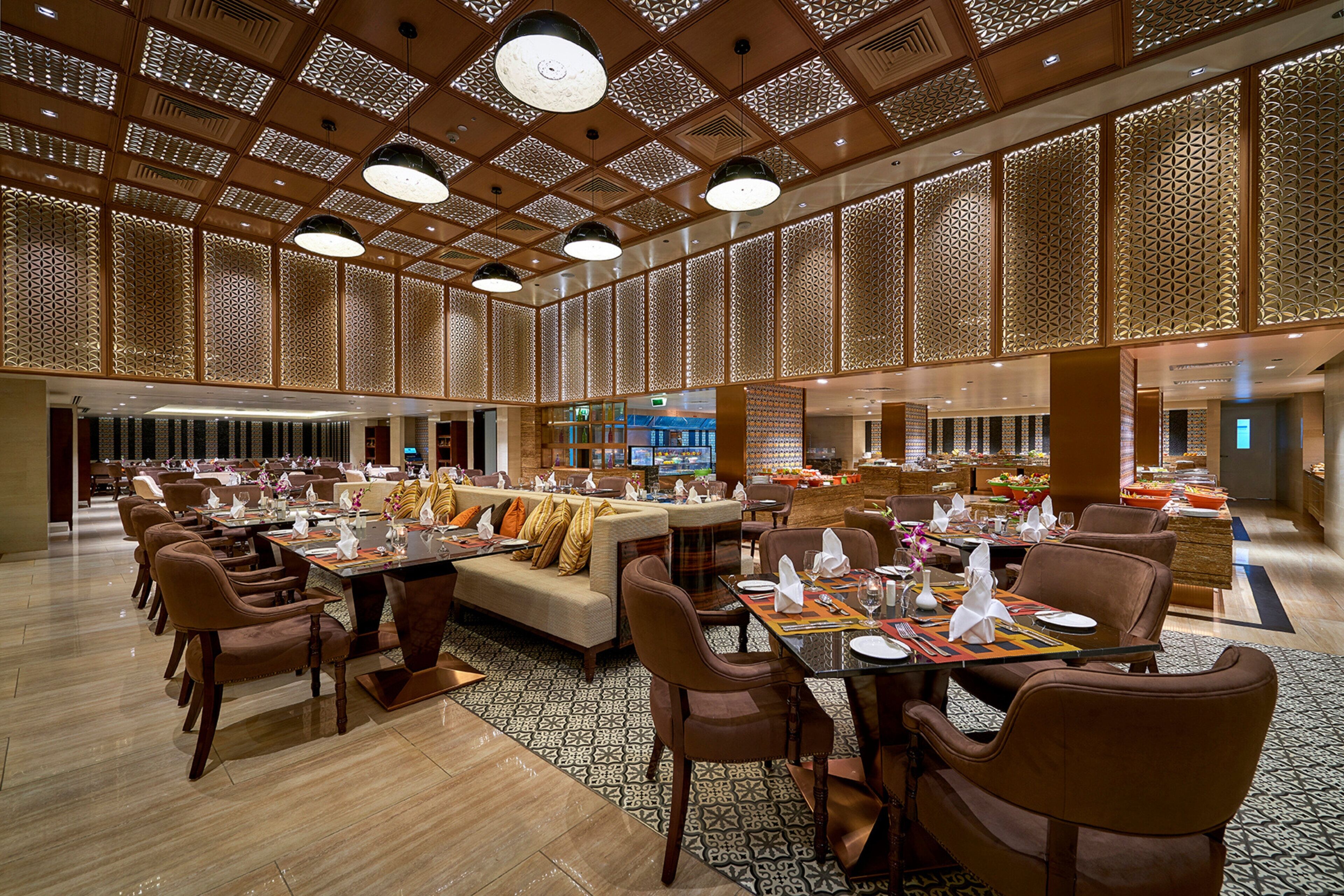 Un vaste espace de restauration dans l’hôtel, offrant différents types d’aménagements, notamment des tables et des canapés, ainsi qu’un bar central.