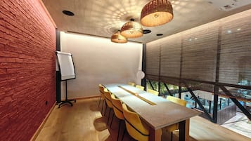 Une salle de conférence avec une longue table, des chaises jaunes, un tableau blanc et une vue sur l’extérieur à travers une fenêtre à motifs.