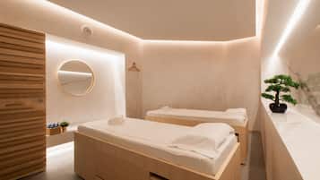 Two single beds with white linens and towels, a wardrobe, mirror, and potted plant.