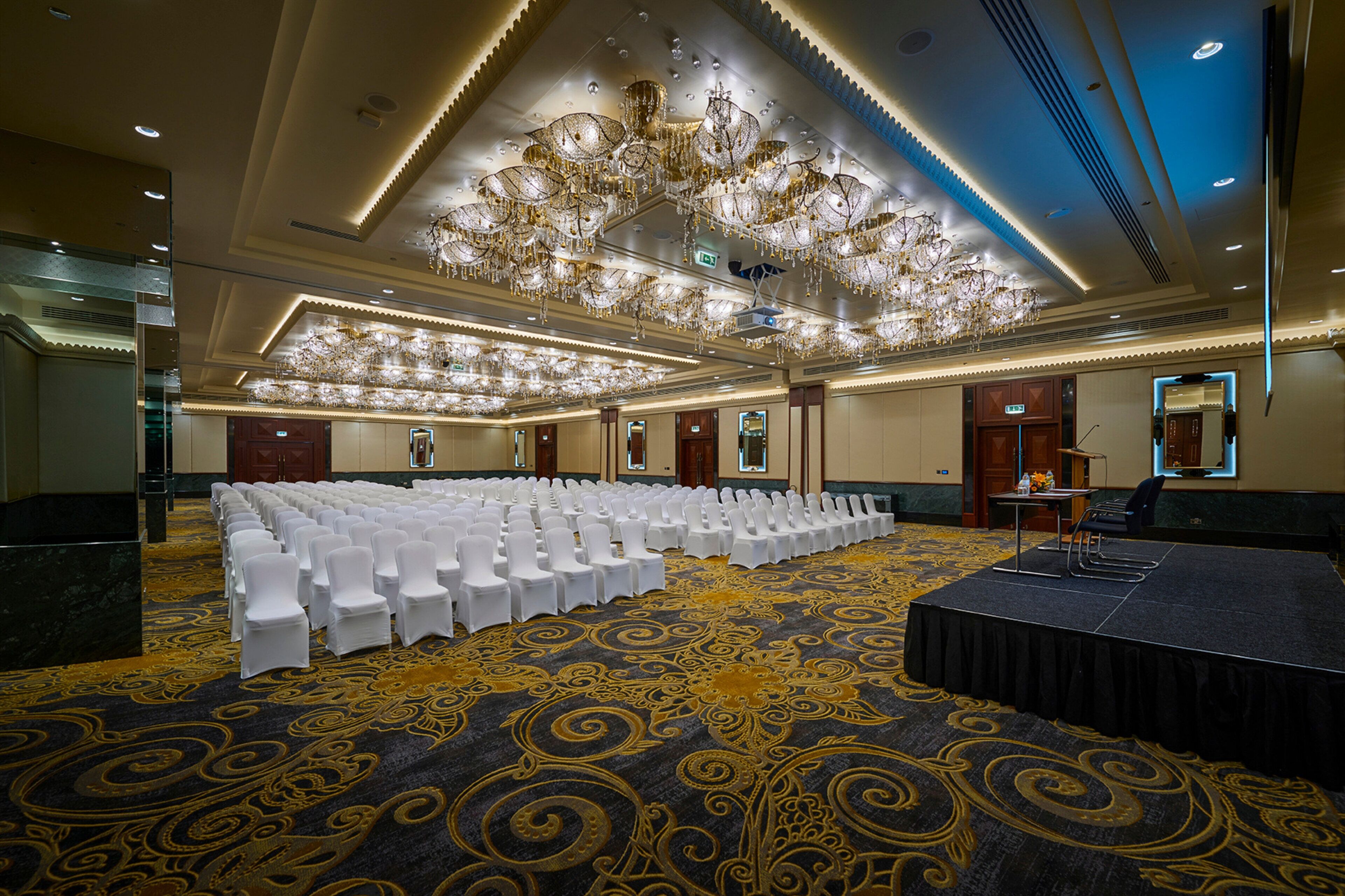 A conference room with rows of white chairs, a stage, and a large chandelier.