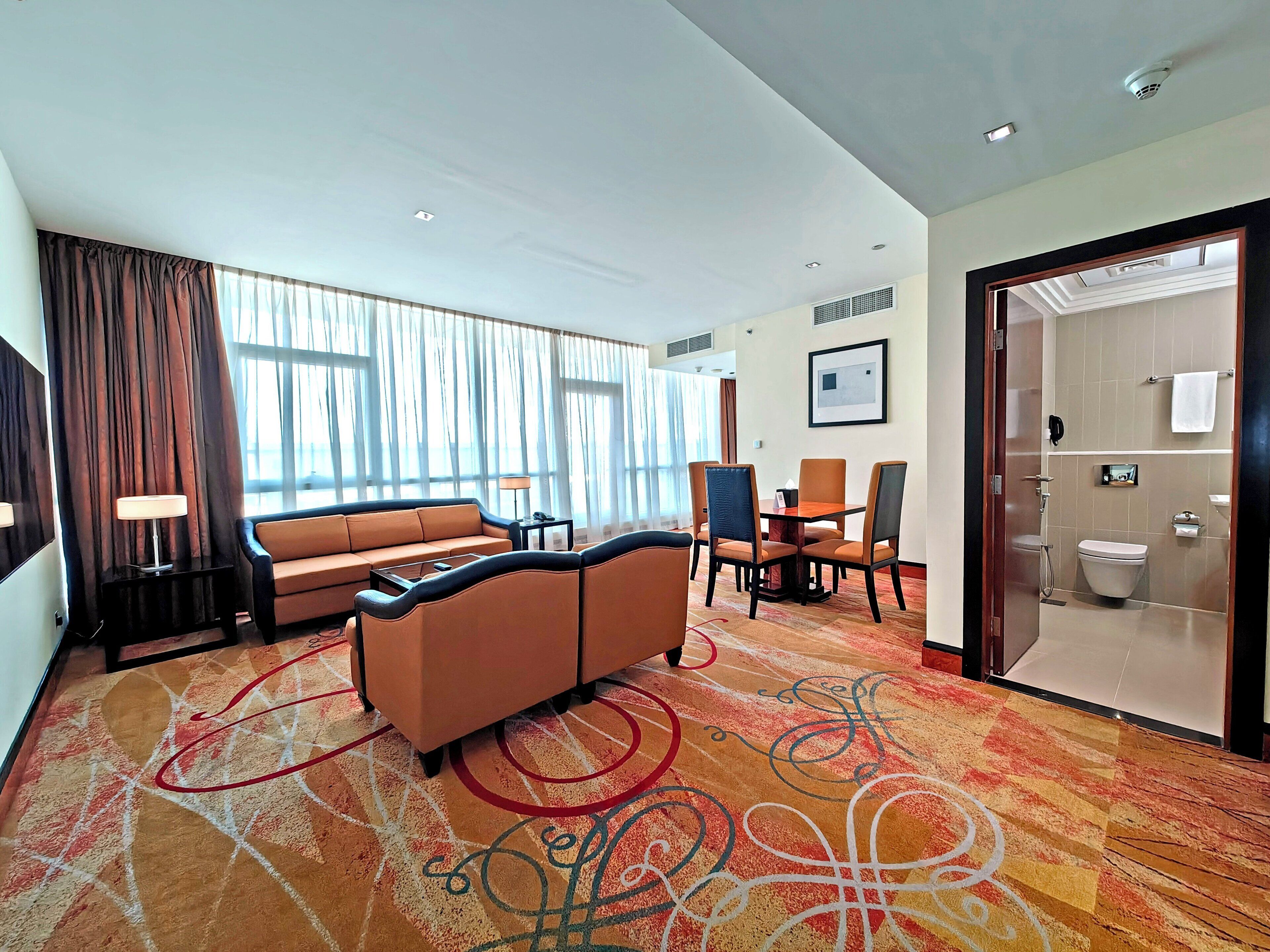 A hotel room with a sofa, chairs, a dining table, and a shower area.