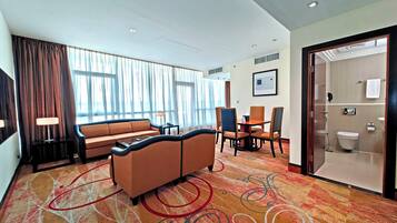 A hotel room with a sofa, chairs, a dining table, and a shower area.