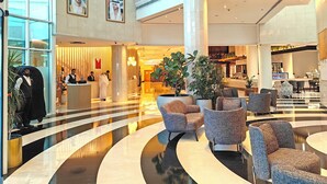 Un vestíbulo amplio con techo alto, ventanas grandes y una zona de recepción con personal.