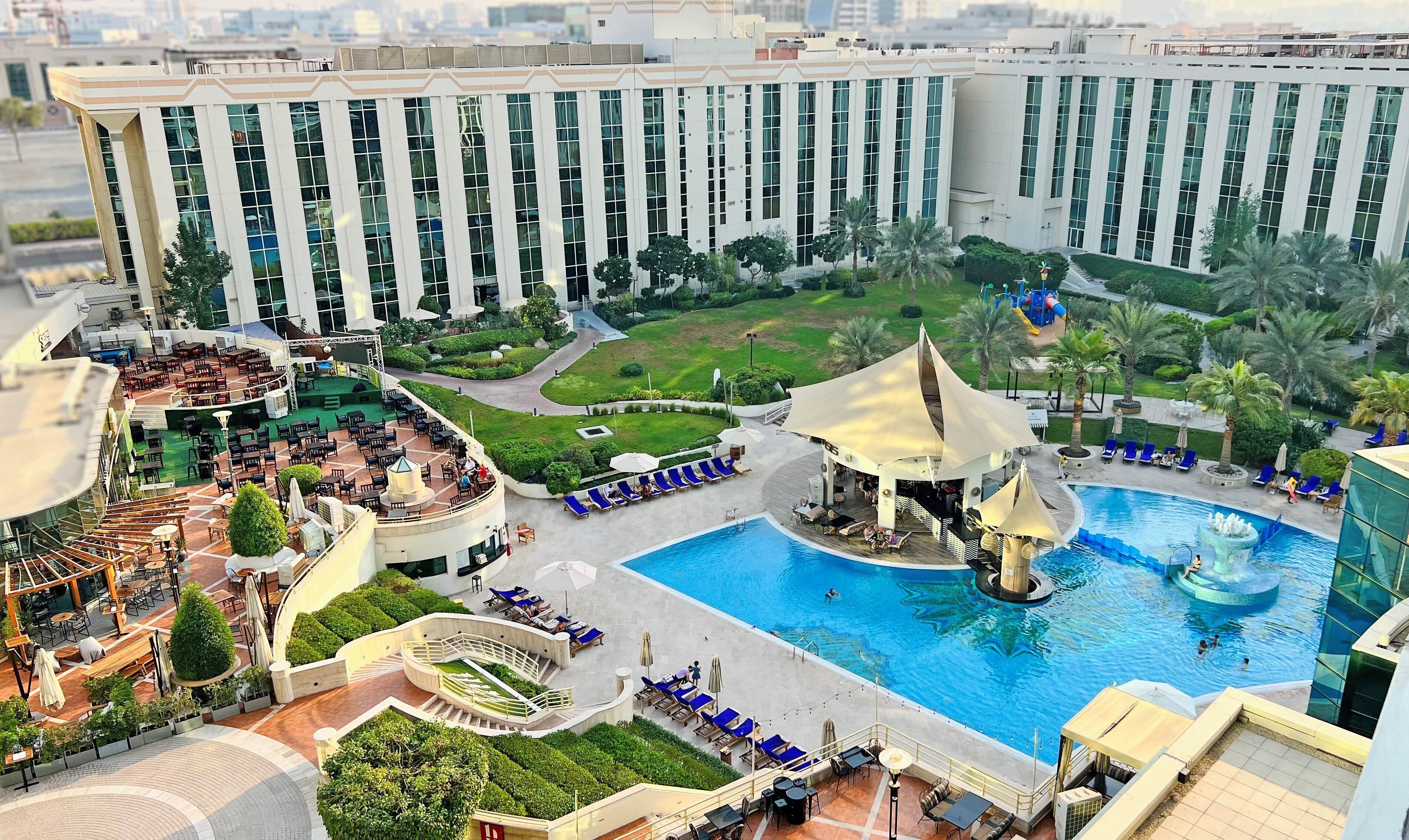 A hotel with a large swimming pool, outdoor seating areas, and a landscaped garden.
