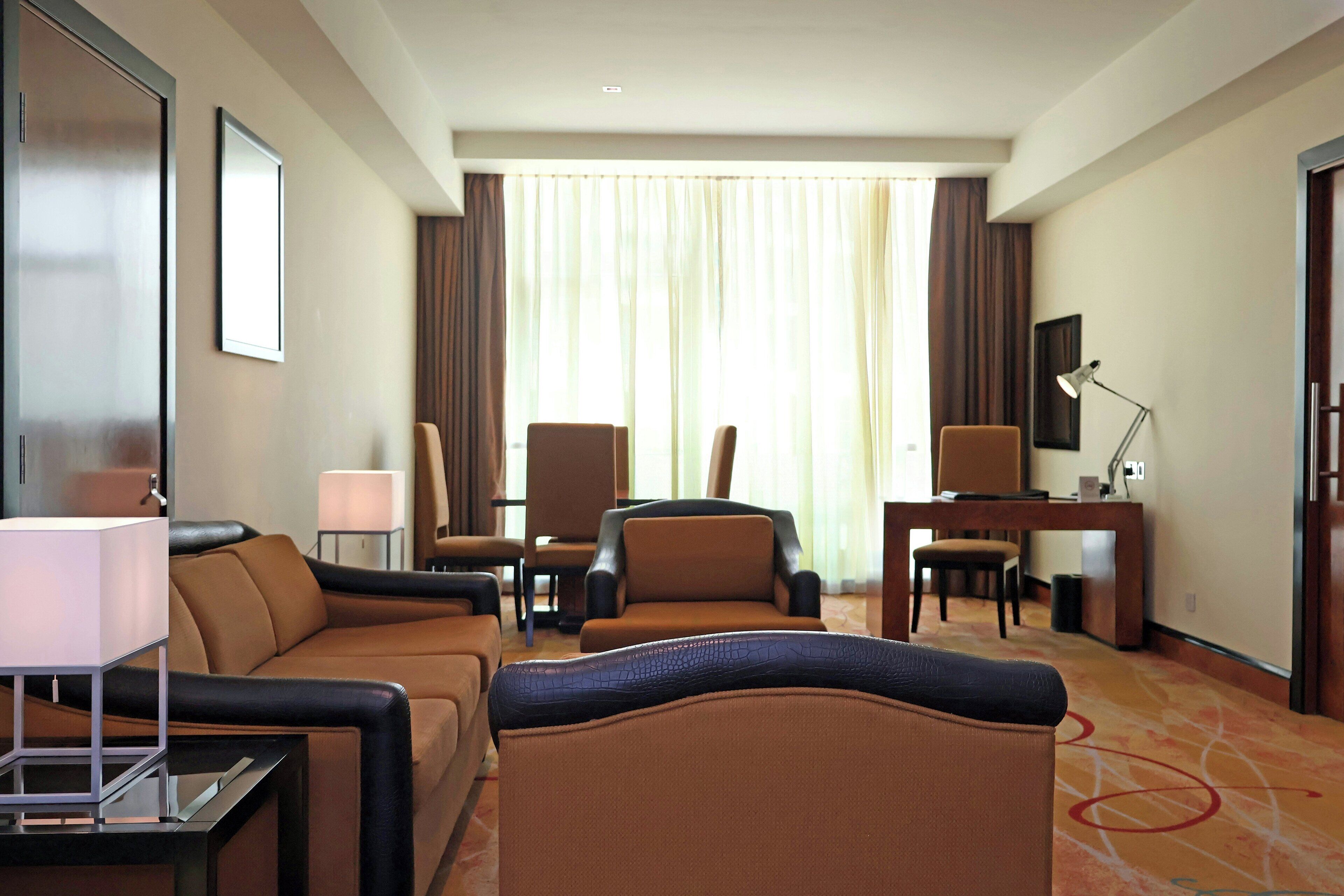 A hotel room with a sofa, two armchairs, a desk, and a television.