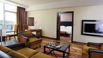 A hotel room with a bed, a desk with a lamp, a TV, and a seating area with a coffee table.
