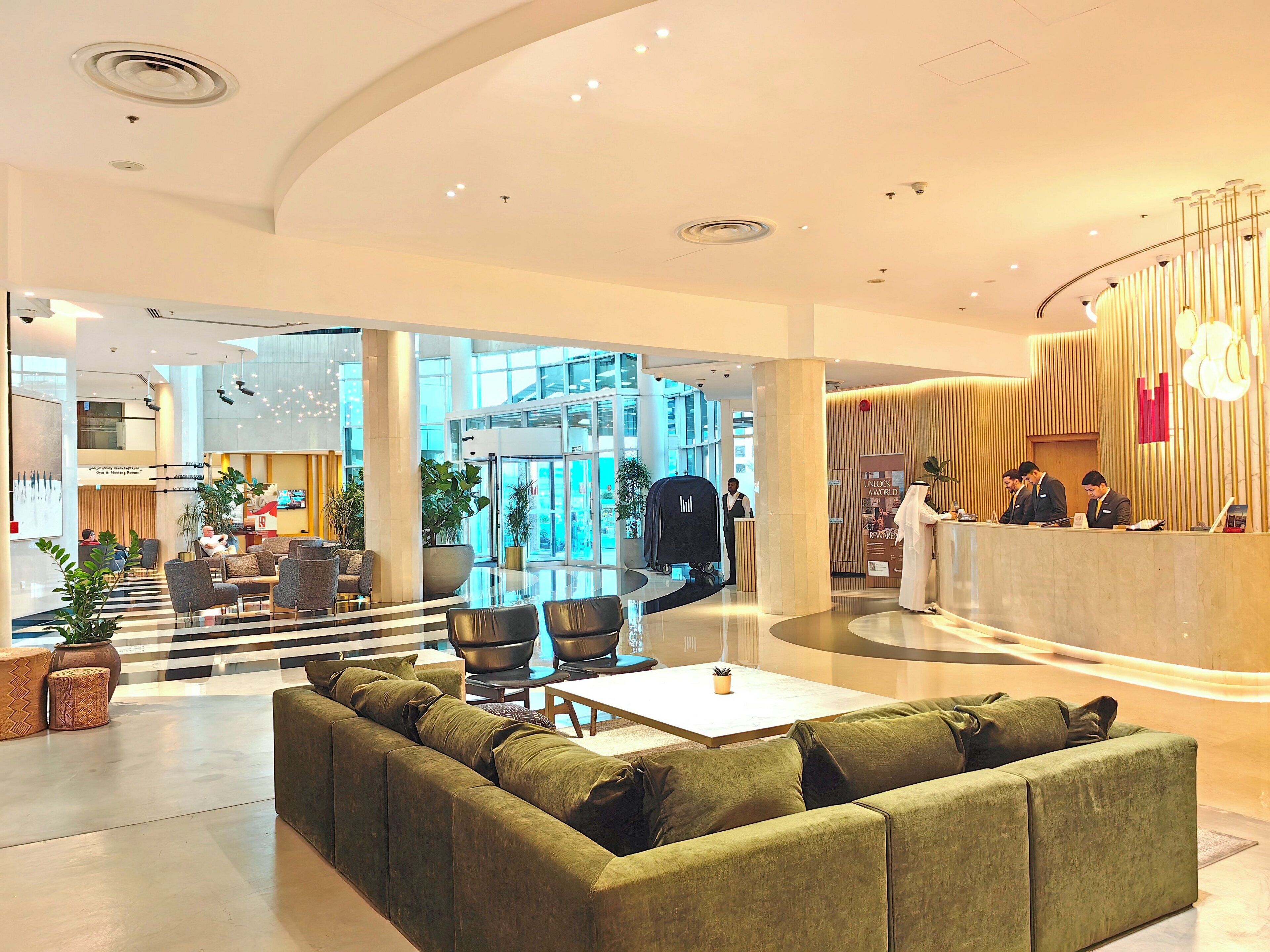 Eine moderne Lobby mit einem grünen Sofa, einem Empfangstresen und einem großen Glastürdurchgang.