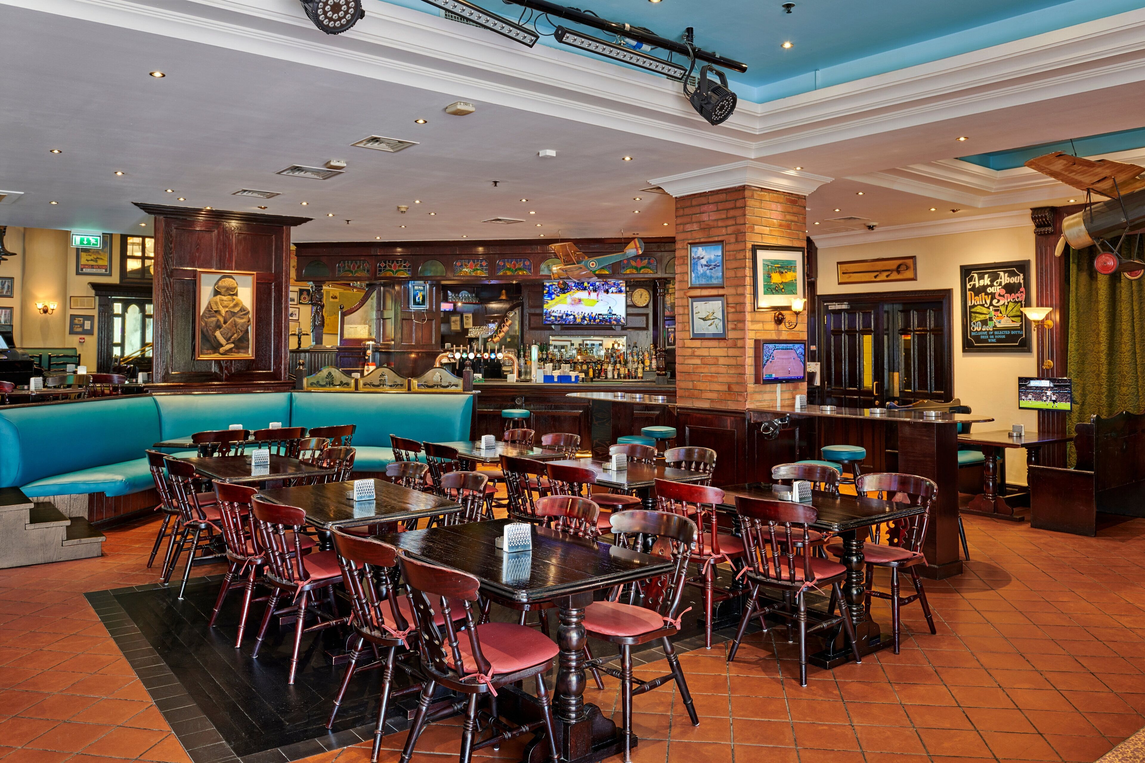 A restaurant with a bar area, multiple tables and chairs, and a blue cushioned seating area.