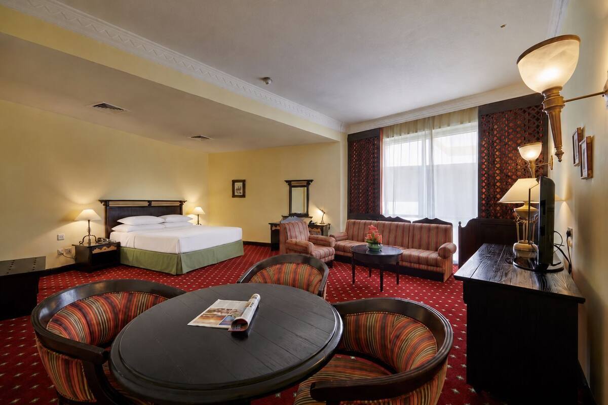 A hotel room with a bed, a sofa, a dining table, and a TV.