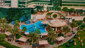 Un hotel con piscina central, mobiliario exterior y un edificio moderno con ventanas de vidrio reflectante.