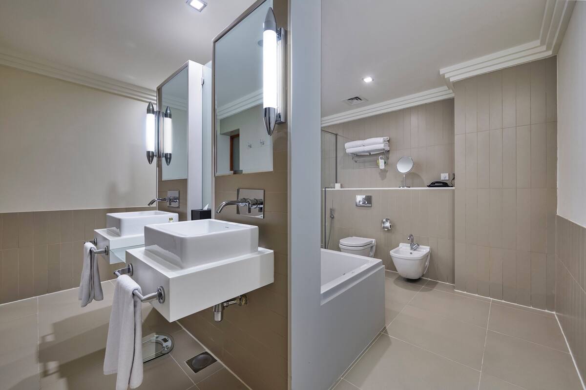A modern bathroom with two sinks, a large mirror, a bathtub, and a toilet.