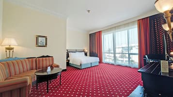 A hotel room with a red carpet, a bed, a sofa, a small table, and a piano.