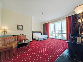 A hotel room with a red carpet, a bed, a sofa, a small table, and a piano.