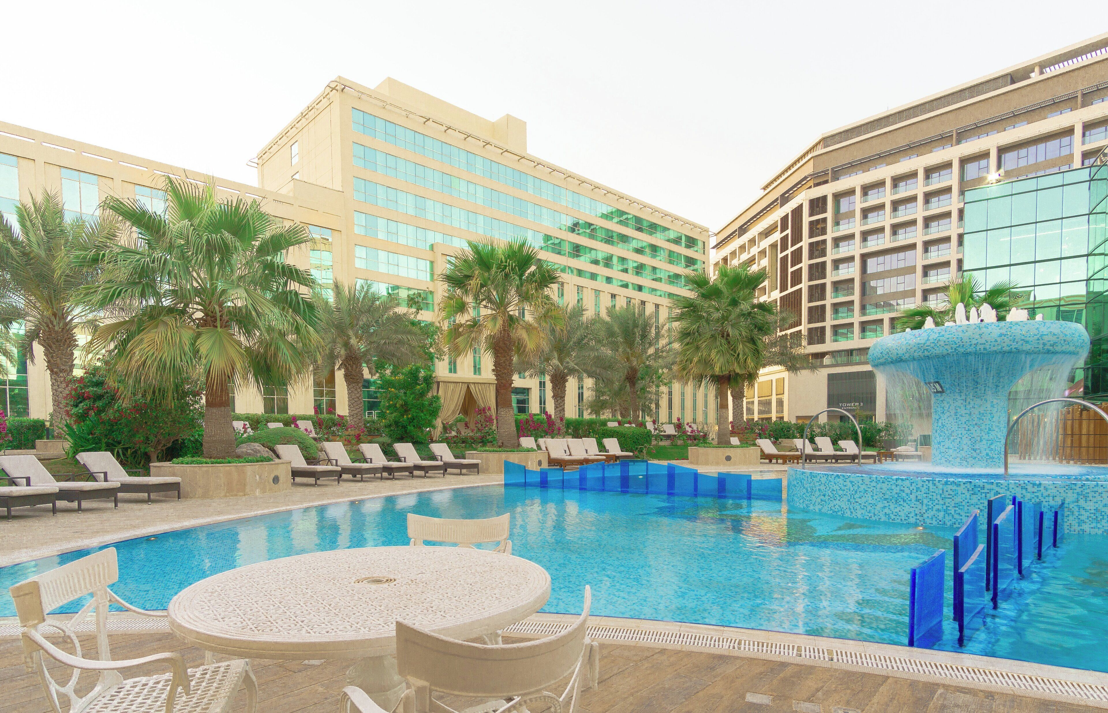 A hotel pool area with lounge chairs, a table, and a fountain.