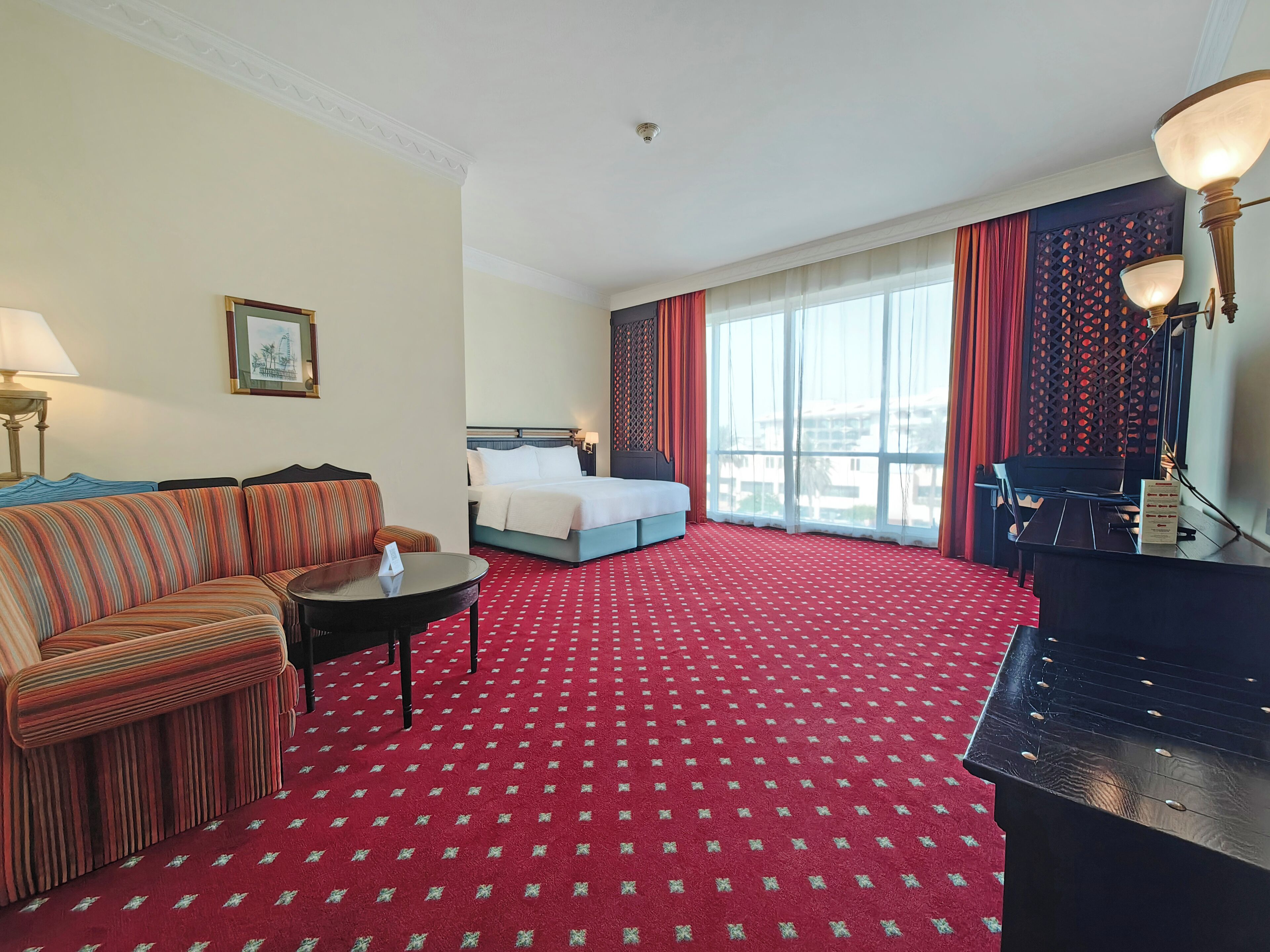 A hotel room with a bed, a sofa, a desk, and a piano.