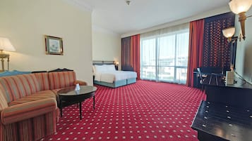A hotel room with a bed, a sofa, a desk, and a piano.