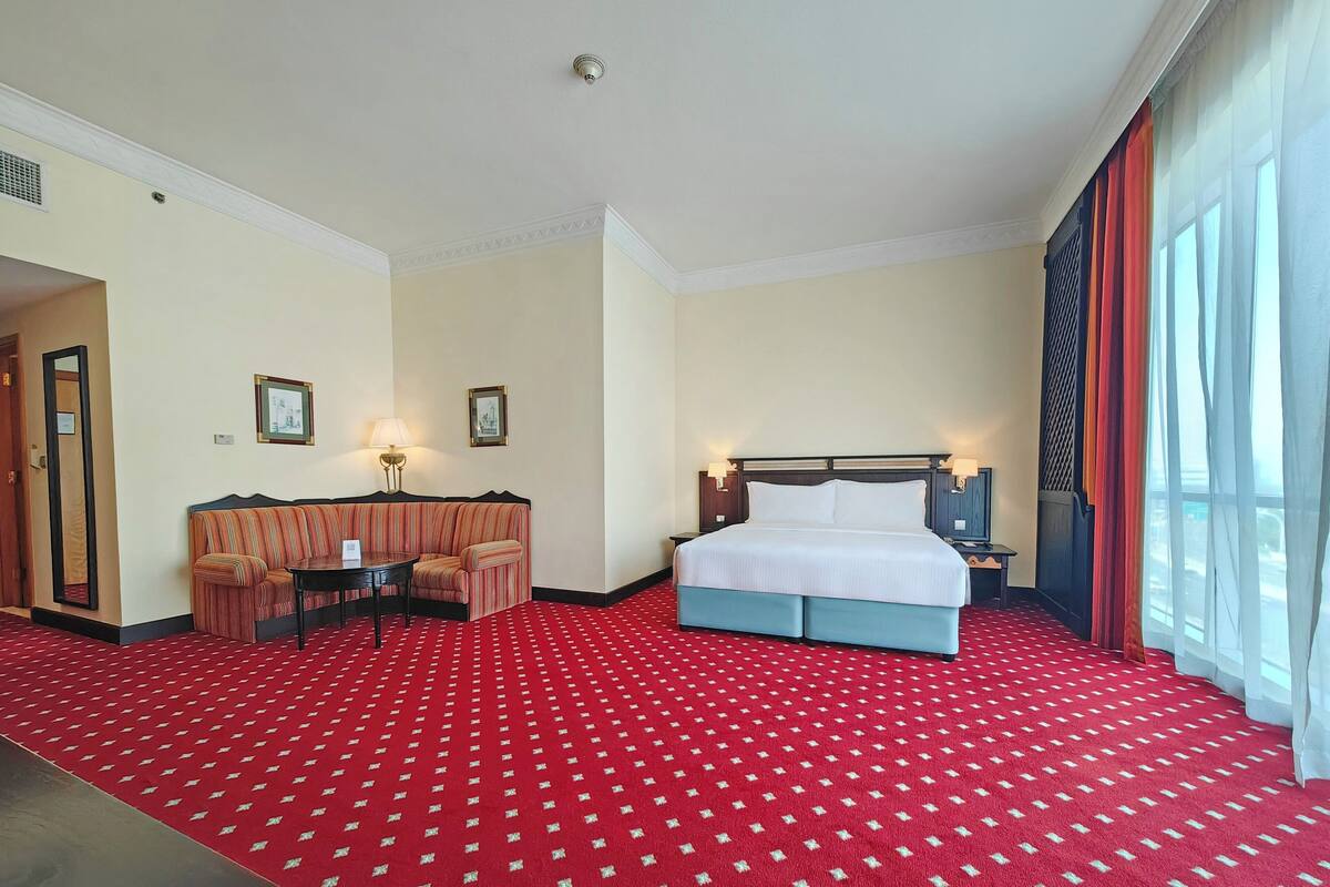 A hotel room with a large bed, a sofa, a desk, and a window with curtains.