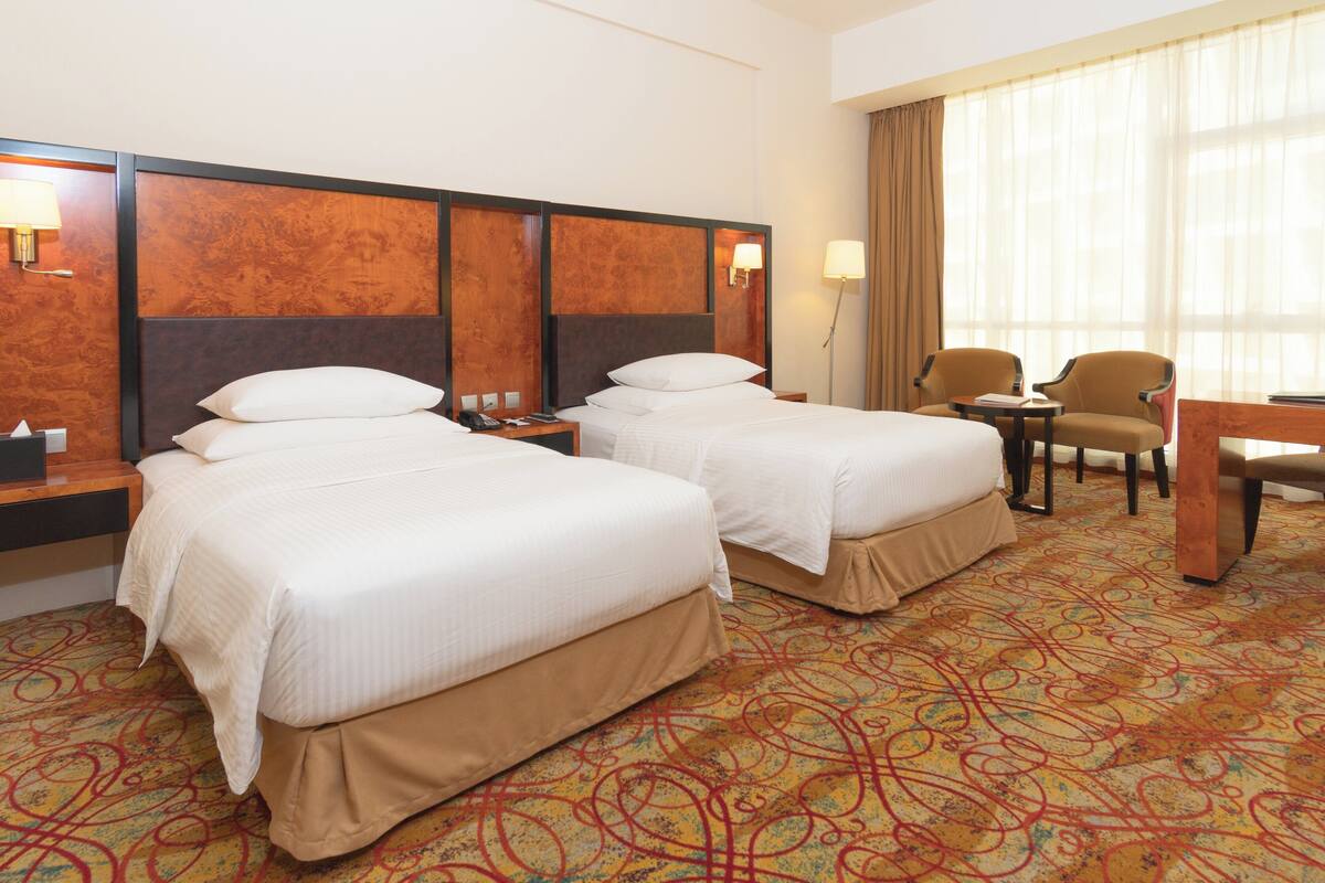 A hotel room with two beds, a desk, and a chair.