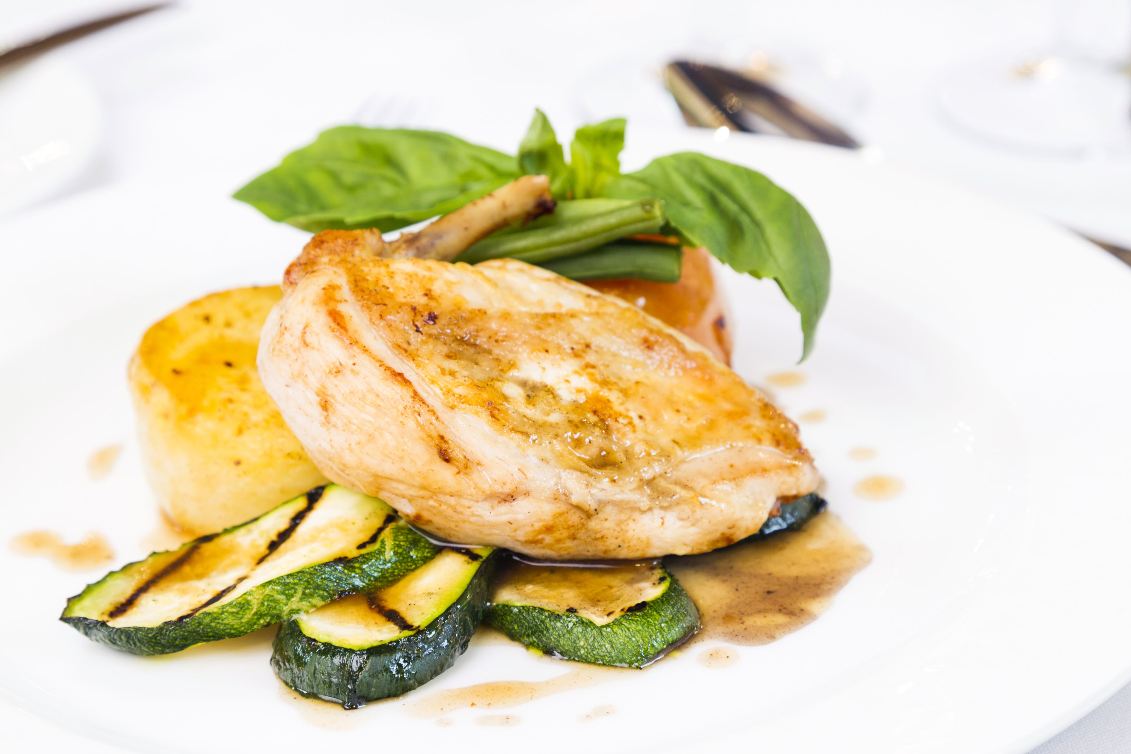 A plate with grilled chicken, zucchini slices, and a garnish of basil leaves.
