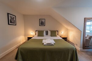 A neatly made bed with a green bedspread and white pillows, two bedside tables with lamps, and framed pictures on the walls.