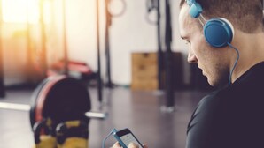 Une personne utilise un smartphone dans une salle de sport, avec des kettlebells et du matériel d’exercice en arrière-plan.
