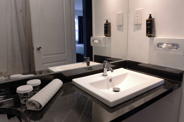 A modern bathroom with a large mirror, a white sink, a towel, and toiletries.