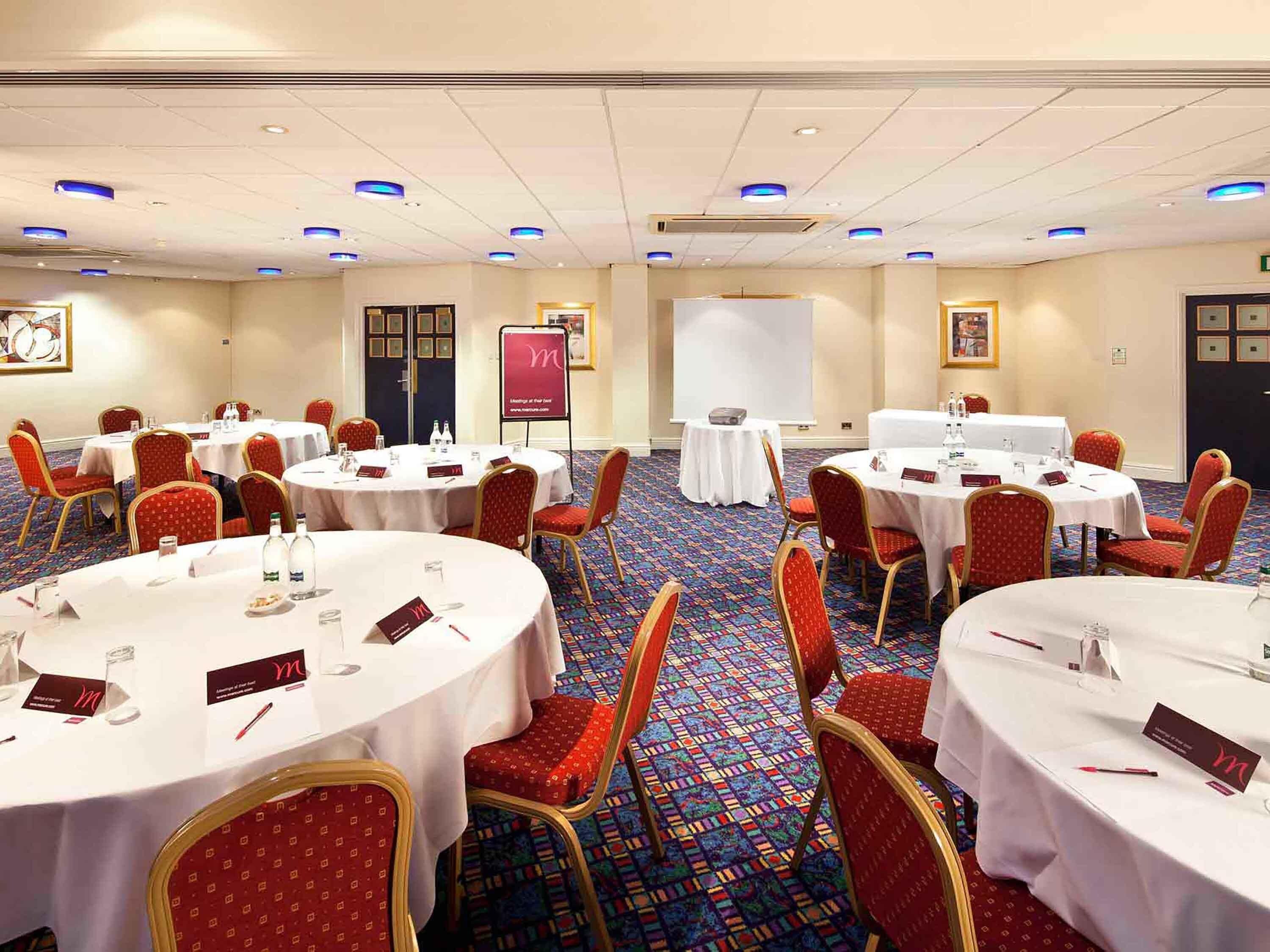 A conference room with round tables, red upholstered chairs, and a carpeted floor.
