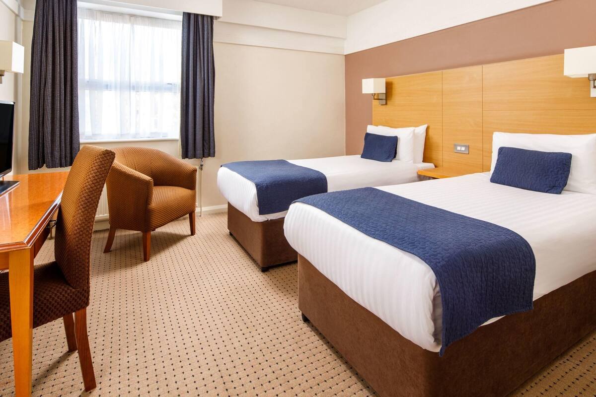 Ein Hotelzimmer mit zwei Betten, einem Schreibtisch, einem Sessel und einem Fernseher.