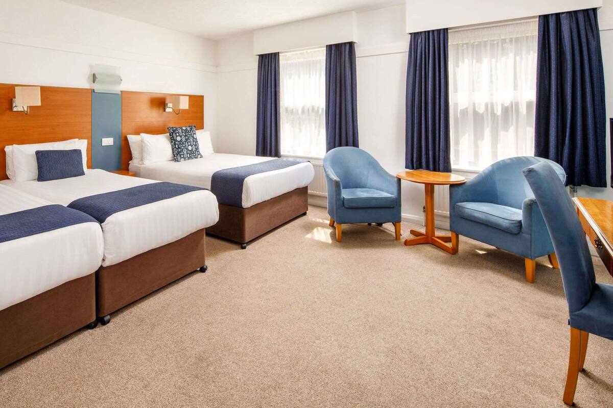Ein Hotelzimmer mit zwei Betten, einem kleinen Tisch, zwei Stühlen und einem Fenster mit Vorhängen.