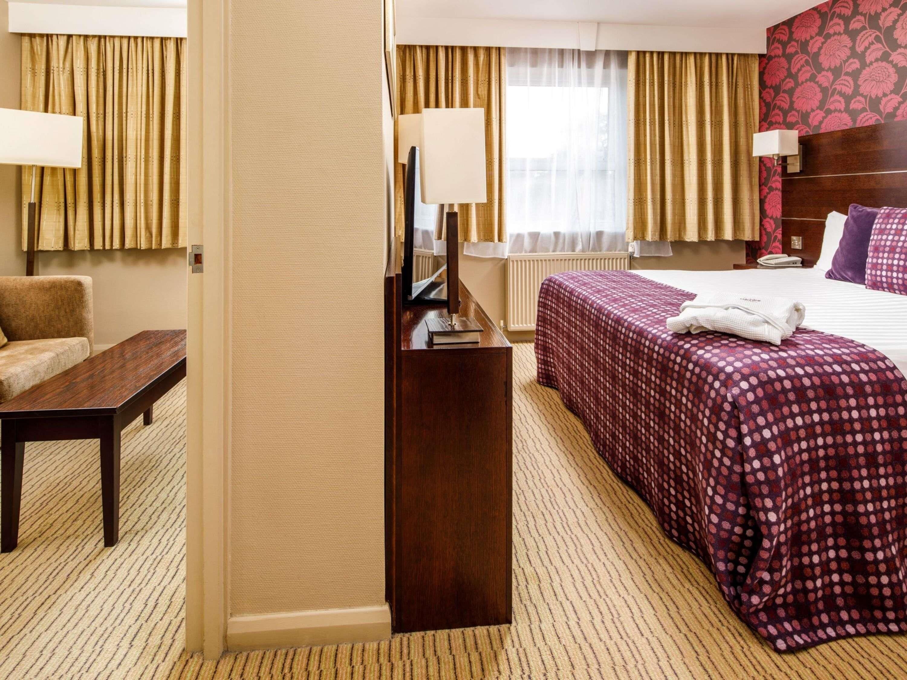 Camera d'albergo con un letto, una scrivania, una sedia e una finestra con tende.