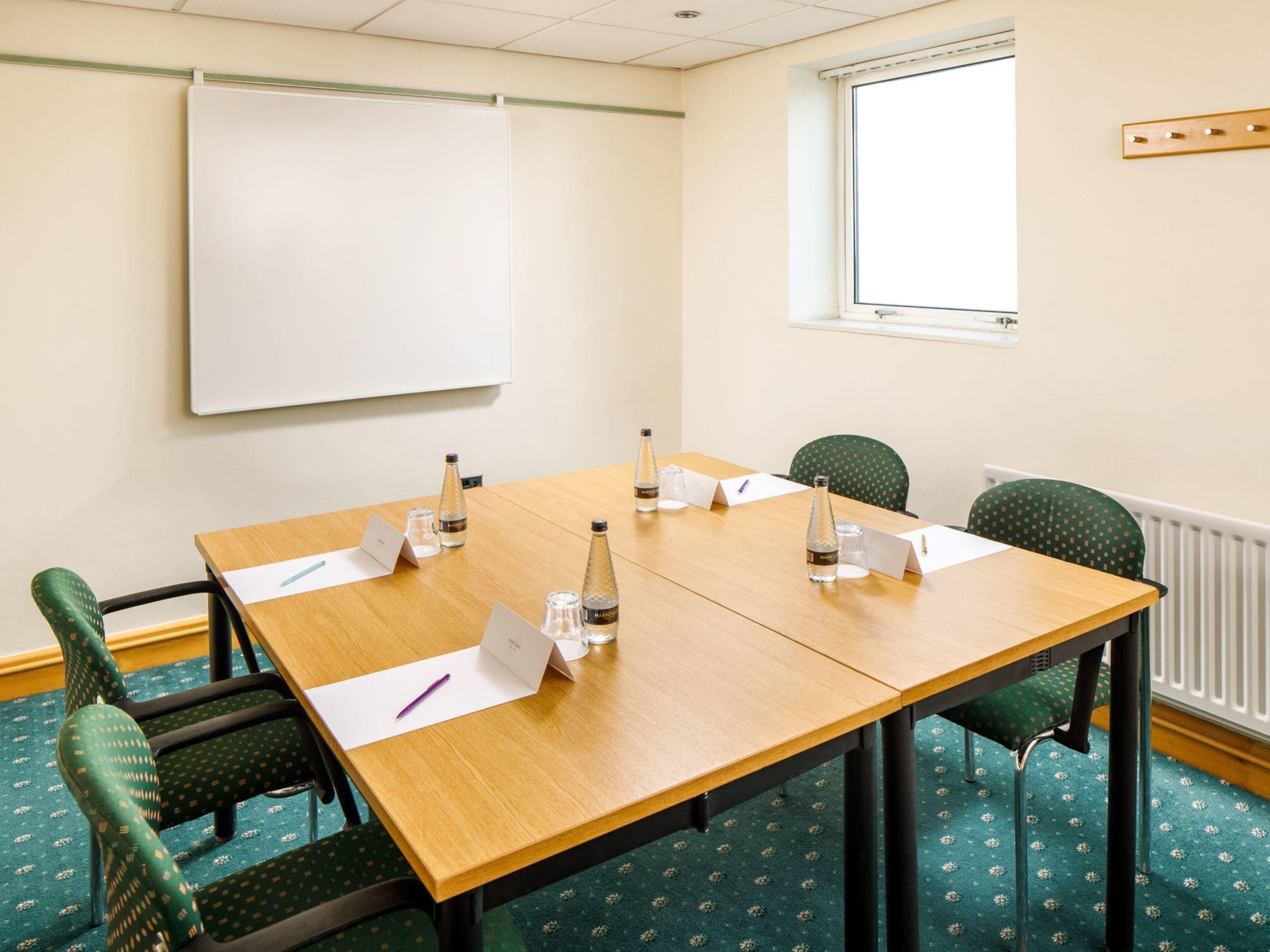 A conference room with a whiteboard, a wooden table, and green patterned chairs.