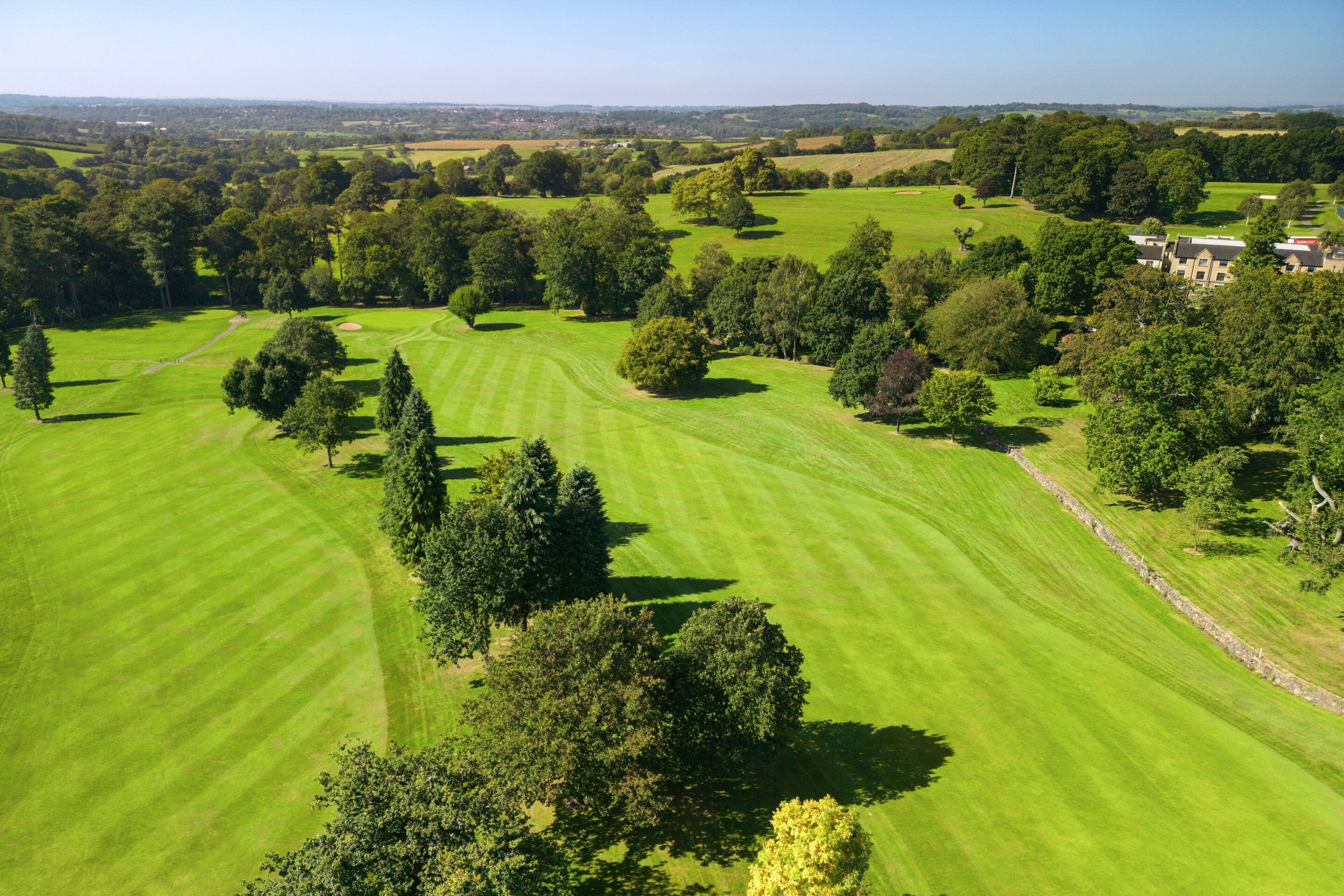 Une vue aérienne d’un terrain de golf avec des verts bien entretenus, des arbres et un bâtiment situé au loin.
