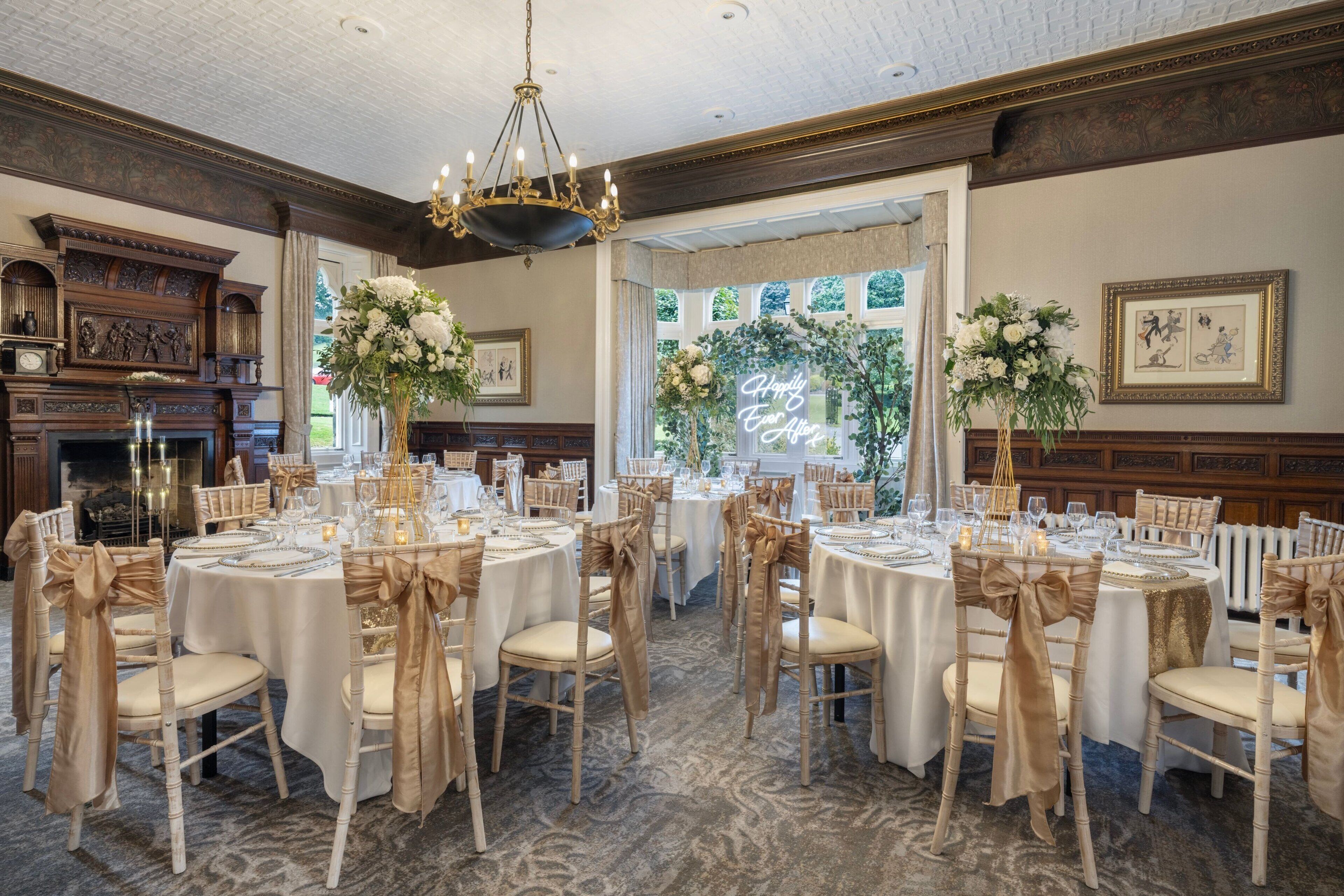A banquet hall with round tables, chairs with gold sashes, and floral centerpieces.