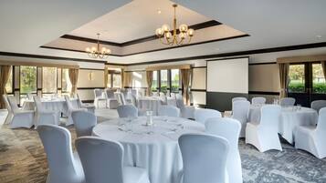 A conference room with round tables, white chairs, and a projector screen.