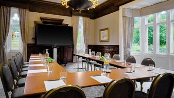 A conference room with a long table, chairs, a television, and windows with curtains.