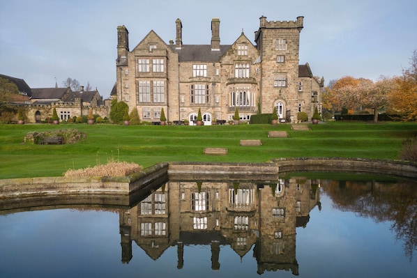 A large stone building with a symmetrical facade, a central entrance, and a reflection in a calm water body in front.