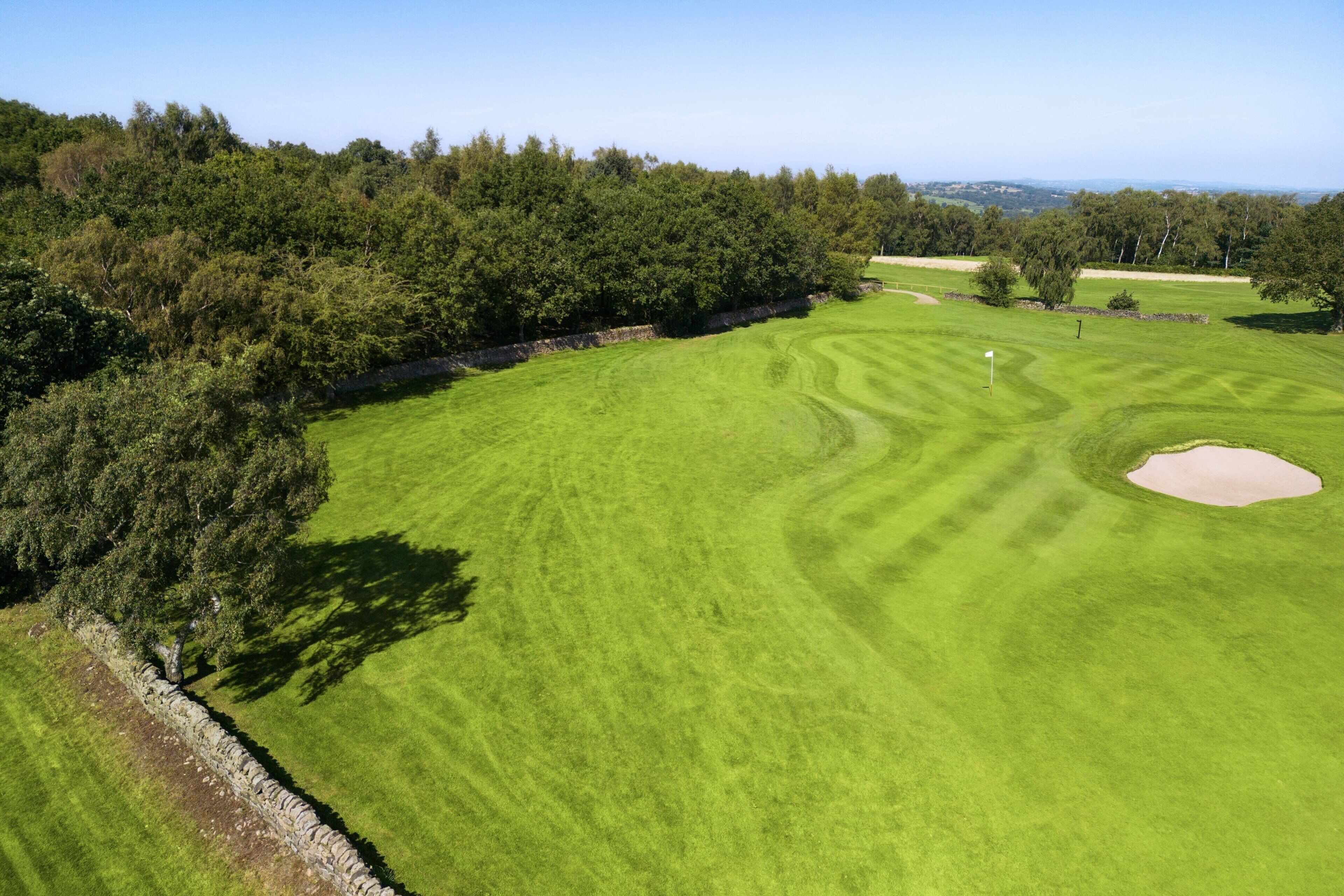 A golf course with a stone wall, trees, and a clear sky.