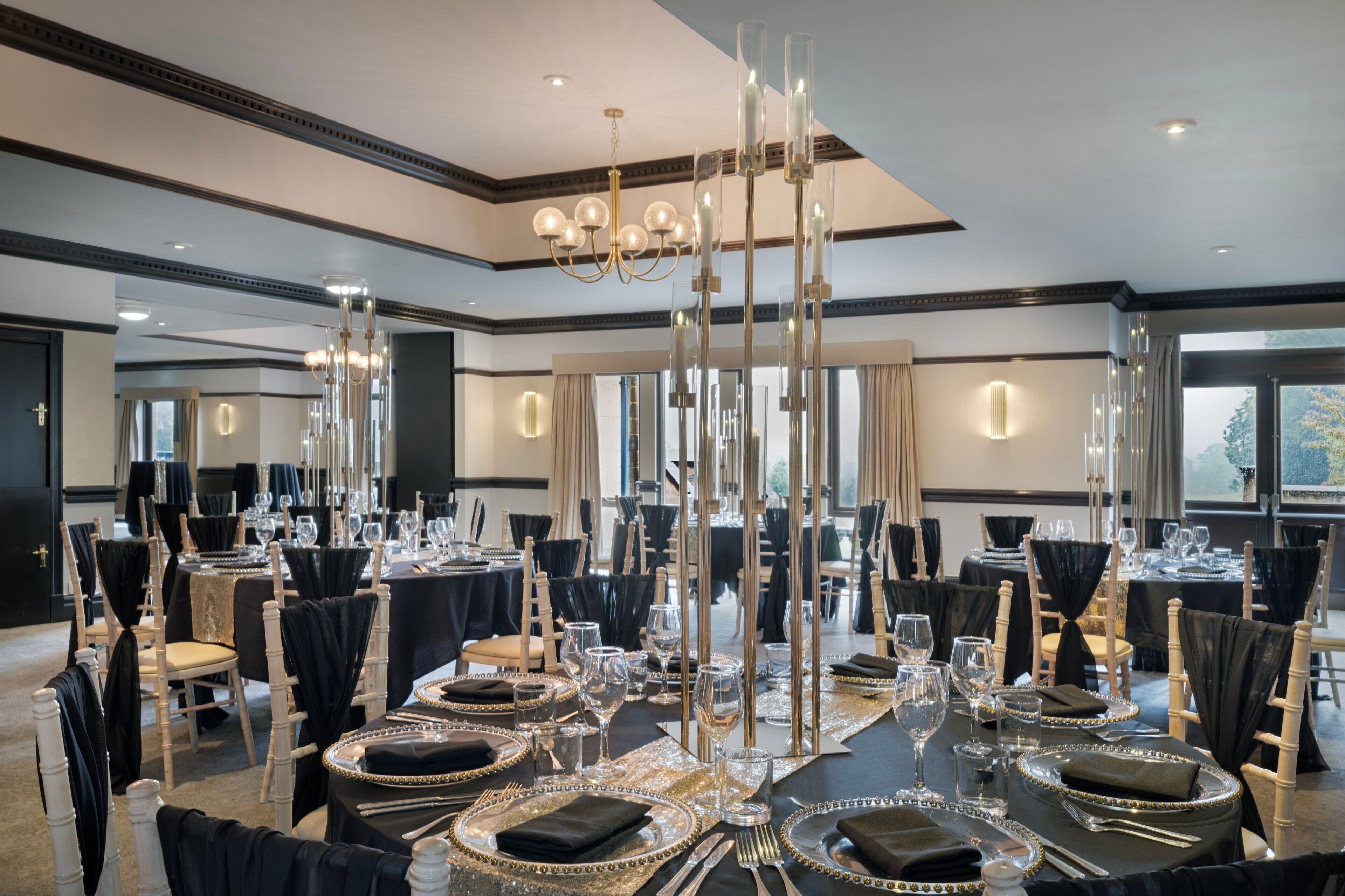 Un salón de banquetes con mesas redondas dispuestas para comer, candelabros altos y un diseño de interiores moderno.